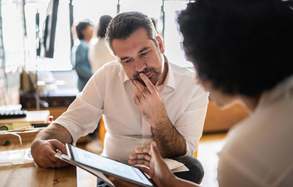 A man sitting opposite a woman puts his index finger over his mouth