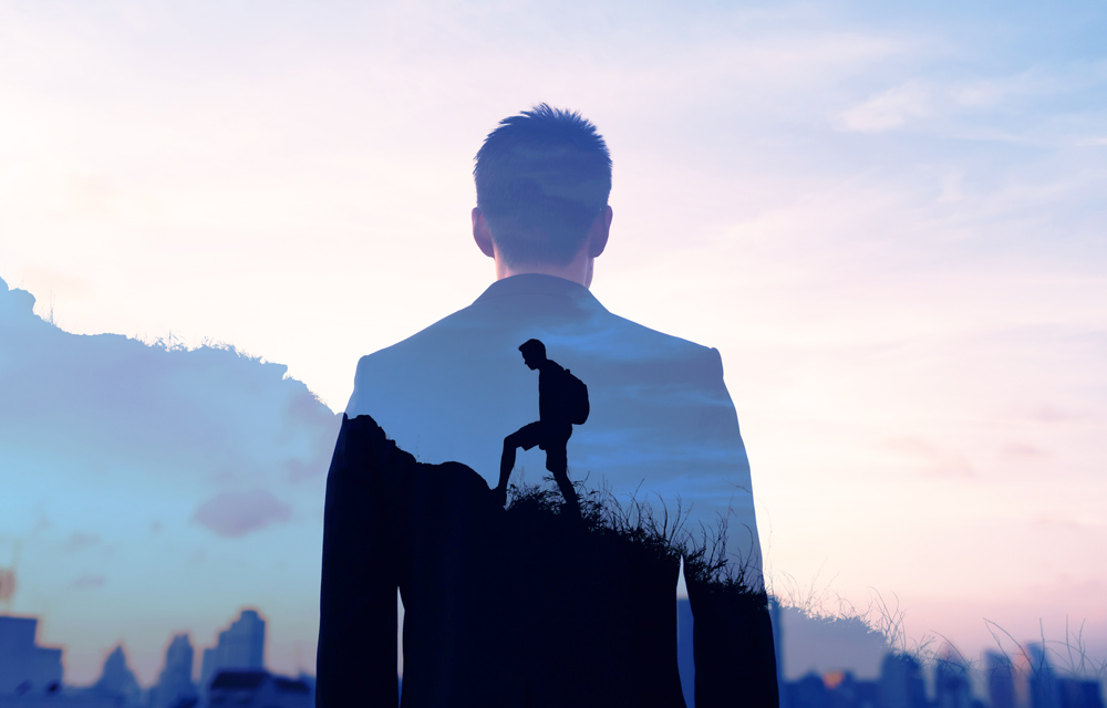 Man in suit stands in front of mountain