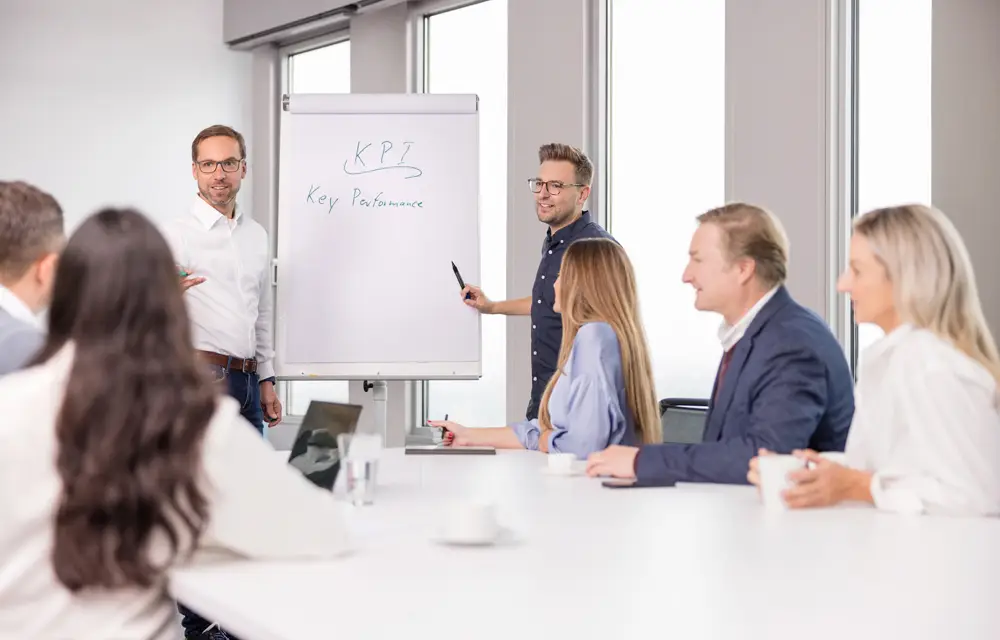 Jan Griesbach und Sven Müller steht vor einem Whiteboard und erklären dem Team etwas